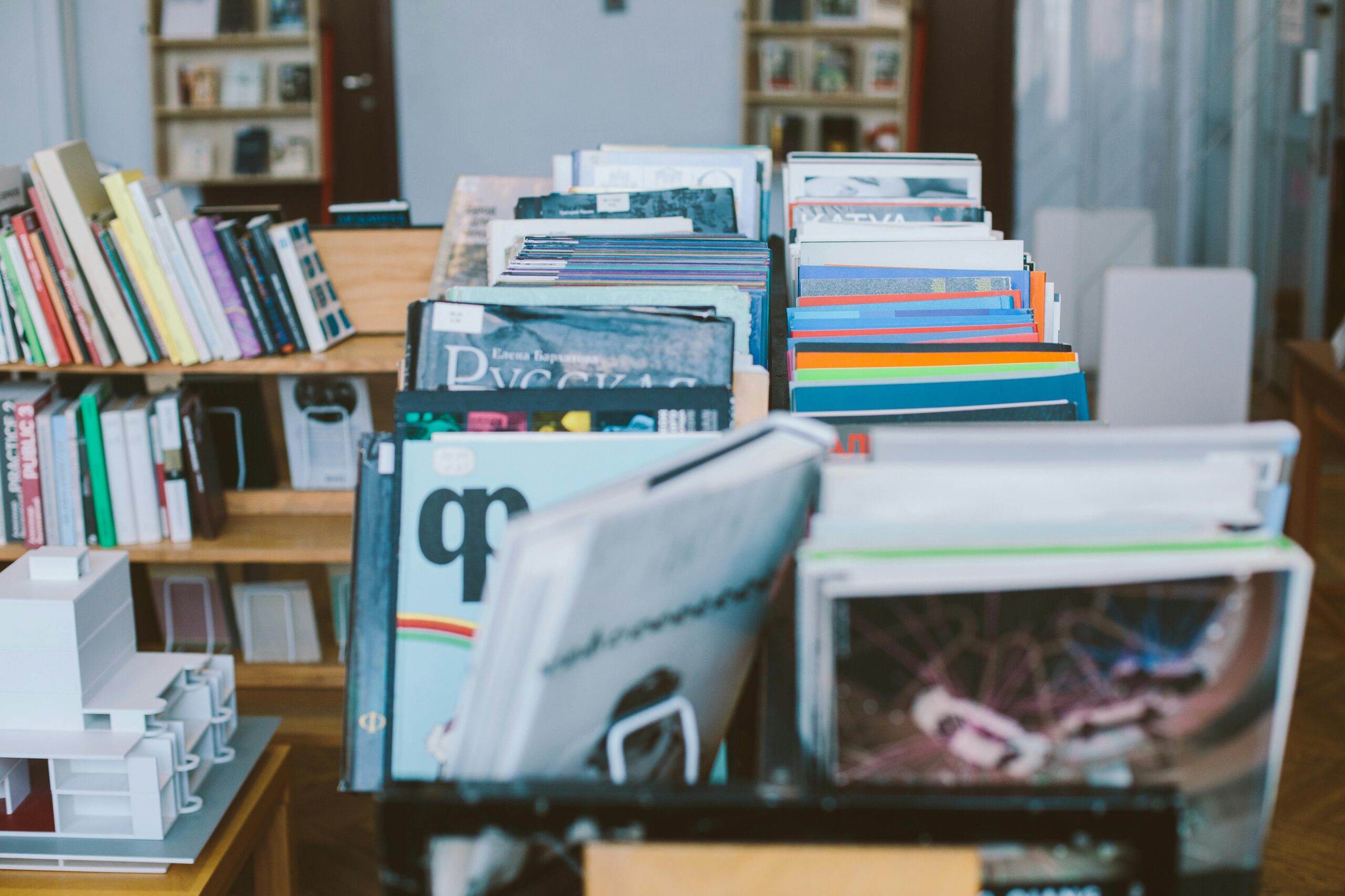 A close-up view of a bookshelf filled with various stacked books and magazines in a library setting.